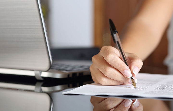 Woman's hand signing documents next to laptop